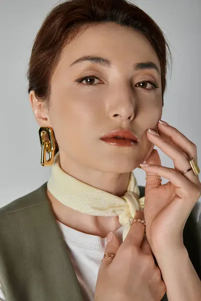 Una mujer con un chaleco elegante y una bufanda en el cuello posa sobre un fondo gris. - foto de stock