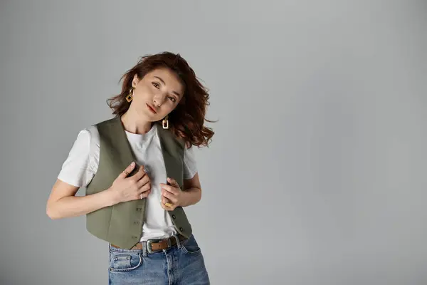 Una mujer asiática elegante en un chaleco verde posa elegantemente sobre un fondo gris, su cabello cayendo flojamente alrededor de sus hombros - foto de stock