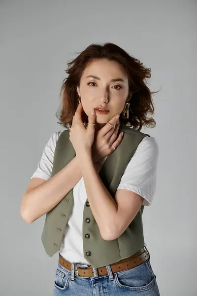A stylish Asian woman in a green vest poses against a grey background. — Stock Photo