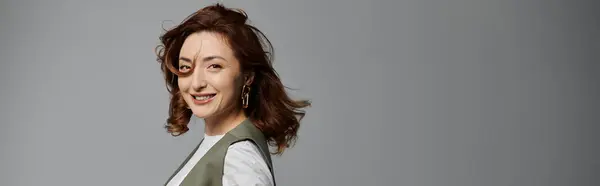 A woman with dark hair, wearing a stylish vest, poses in front of a grey background, her hair flowing and her smile bright. — Stock Photo