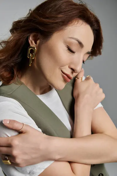 A stylish Asian woman with long brown hair and a warm smile is wrapped in her arms while wearing a vest — Stock Photo
