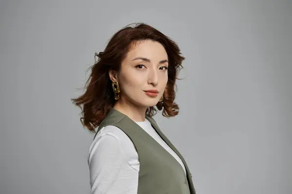 Красивая азиатка с темно-коричневыми волосами позирует в зеленом жилете на сером фоне. — стоковое фото