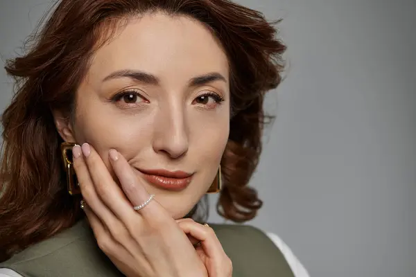 Una bella donna asiatica con lunghi capelli castani posa in un gilet elegante, la sua mano poggia delicatamente sulla guancia. — Foto stock