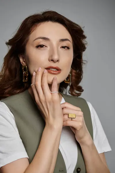 Stylish Asian woman with brown hair poses in a green vest, delicately placing her hands near her face to accentuate beauty — Stock Photo