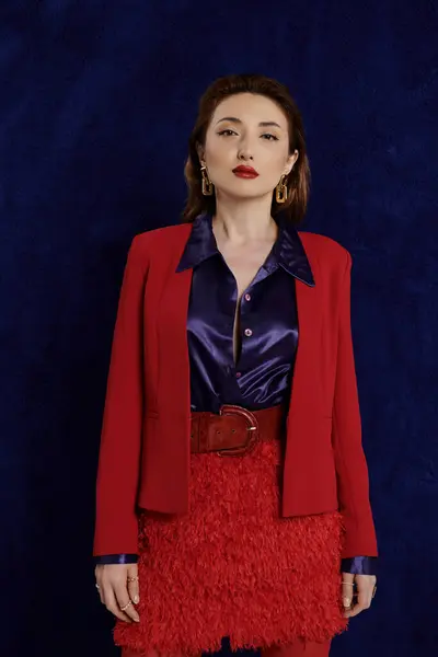 An Asian woman in a red suit poses confidently against a dark blue background, creating a striking image — Stock Photo