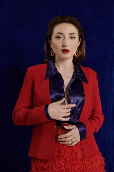 A stylish and attractive Asian woman poses in a red suit and silk shirt against a dark background, radiating confidence and elegance. — Stock Photo