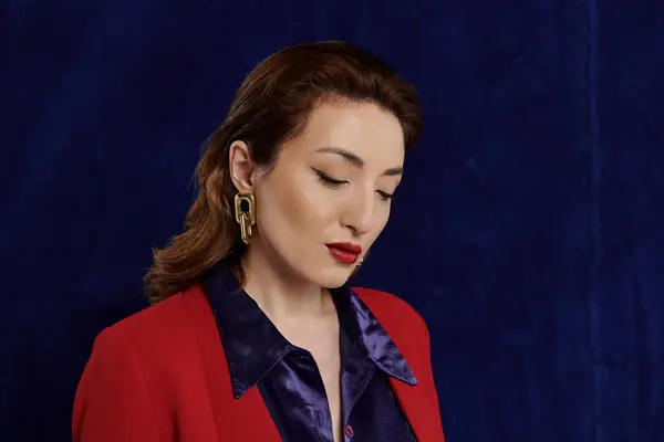 A stylish Asian woman in a crimson suit and a silky blue shirt poses against a navy blue background. — Stock Photo