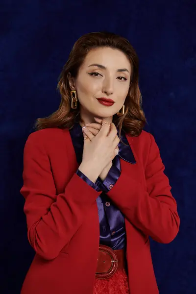 A woman in a red suit with a silk shirt poses against a dark background. — Stock Photo