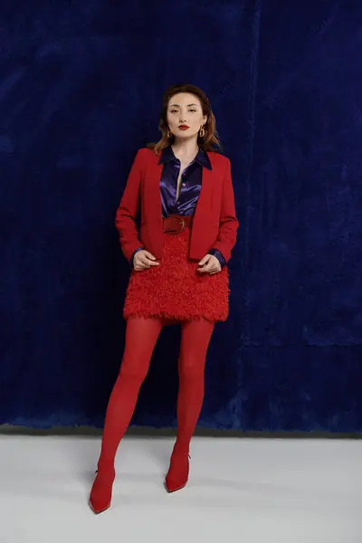 A woman in a red suit and silk shirt poses against a dark blue backdrop, radiating confidence and style. — Stock Photo