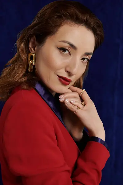 A stylish Asian woman in a bold red suit and a silky shirt poses against a dark background, her eyes sparkling with confidence. — Stock Photo