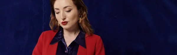 Una mujer asiática elegante que viste un traje rojo y una camisa de seda posa sobre un telón de fondo azul oscuro. - foto de stock