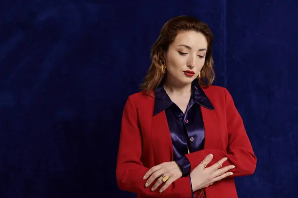 An attractive Asian woman poses in a red suit, her arms crossed, against a deep blue backdrop. — Stock Photo