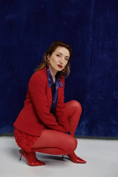 A stylish Asian woman in a red suit and silk shirt poses against a dark blue background. — Stock Photo