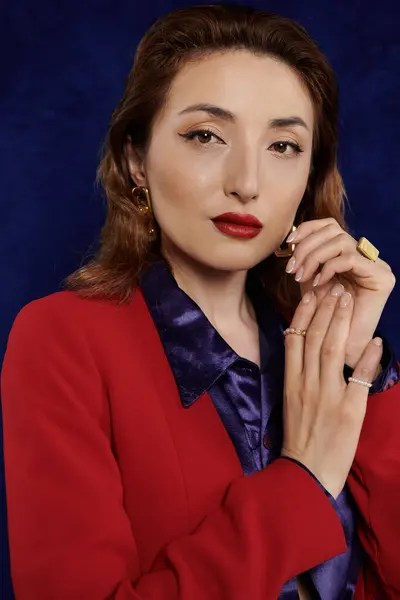 Una donna in abito rosso e una camicia di seta posa su uno sfondo scuro, trasudando fiducia e stile. — Foto stock