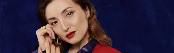 An attractive Asian woman poses, her red suit set against a dark blue background. — Stock Photo