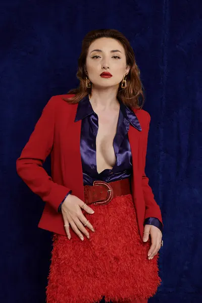 A stylish Asian woman in a red suit and silk shirt poses confidently against a dark background. — Stock Photo