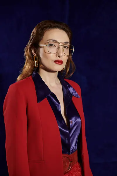 A stylish Asian woman in a red blazer and silk shirt poses confidently against a dark background. — Stock Photo