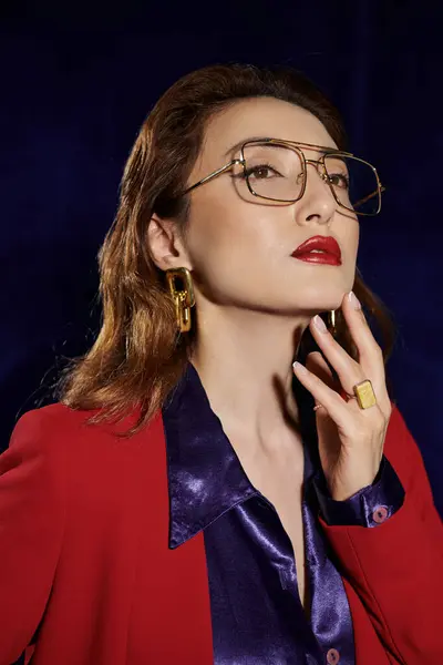 An Asian woman in a red suit and a silk shirt gazes confidently upward, her gold jewelry catching the light. — Stock Photo