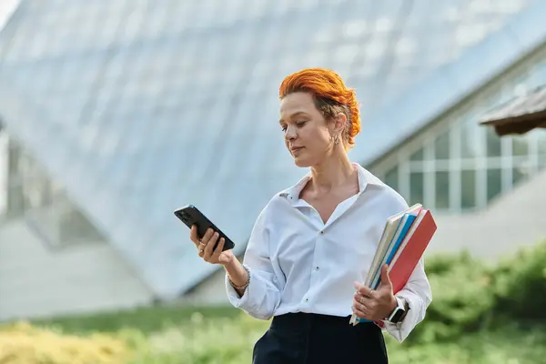 A teacher with bright red hair checks her phone on campus. — Stock Photo