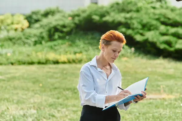 Mujer joven con el pelo rojo en camisa blanca escribe al aire libre — Stock Photo