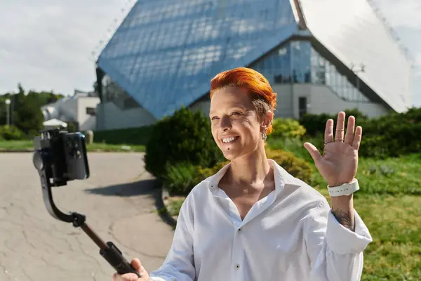 A woman with red hair smiles and waves at the camera on a bright, sunny day. — Stock Photo