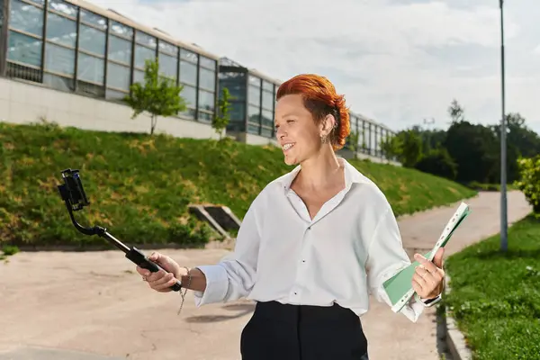A teacher holds a selfie stick and smiles for the camera while walking on campus. — Stock Photo
