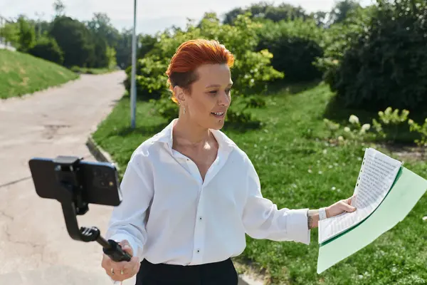 A young teacher walks and films on campus, holding notes. — Stock Photo