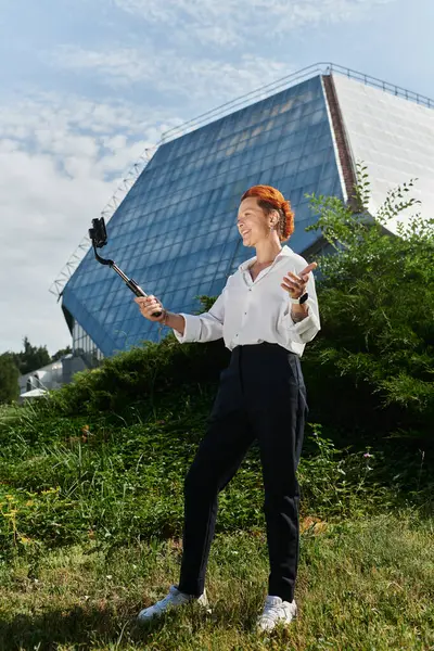 A teacher in a white shirt and black pants takes a selfie with a selfie stick on a sunny day. — Stock Photo