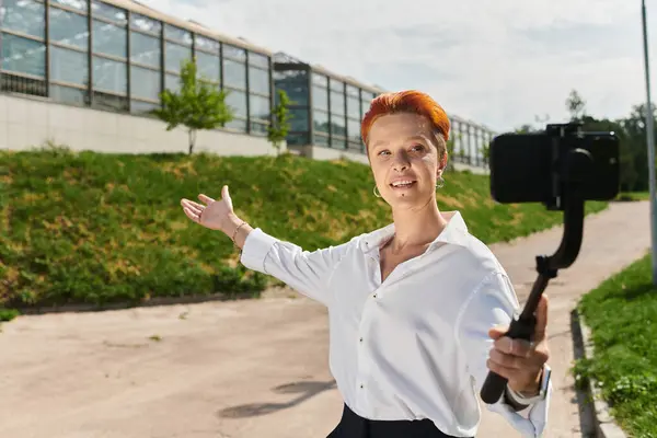 A teacher in a white shirt smiles while recording a selfie video on a sunny campus. — Stock Photo