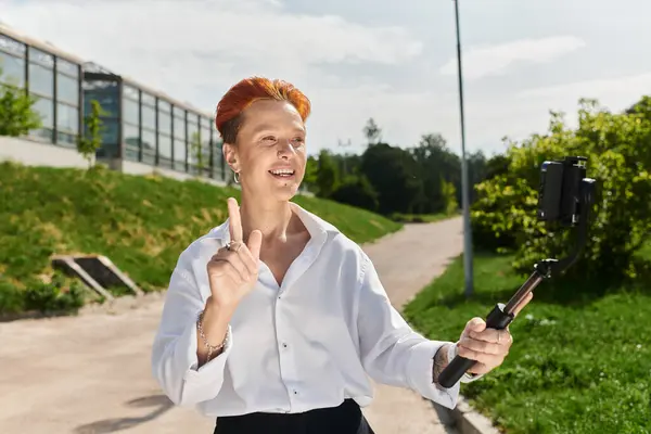 A teacher with orange hair films a vlog while walking on a campus path. — Stock Photo