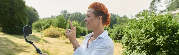 Une femme aux cheveux roux et à la chemise blanche filme une vidéo en plein air sur un campus universitaire. — Photo de stock