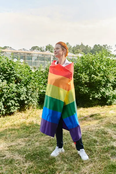 Eine Frau steht stolz in eine Regenbogenfahne gehüllt auf einem grasbewachsenen Campus. — Stockfoto