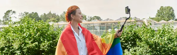 A woman draped in a rainbow flag smiles while taking a selfie on a university campus. — Stock Photo