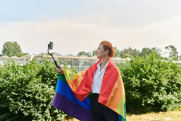 A woman in a white shirt takes a selfie with a rainbow flag draped around her. — Stock Photo