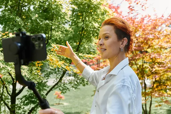 Un jeune professeur enregistre une vidéo sur un campus ensoleillé, entouré de feuillage. — Photo de stock