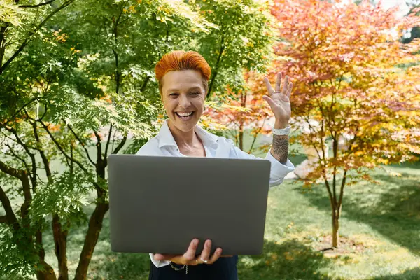 A teacher in a white shirt smiles and waves while holding a laptop in front of her. — Stock Photo