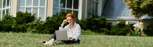 A teacher sits on the grass, using a laptop. — Stock Photo