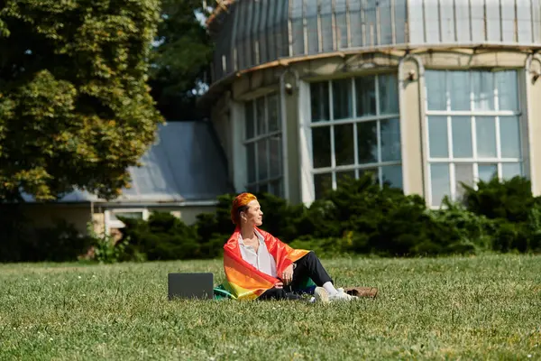 Un enseignant enveloppé dans un drapeau arc-en-ciel se détend sur l'herbe à l'extérieur d'un bâtiment du campus. — Photo de stock