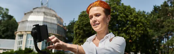 Una joven con el pelo rojo se toma una selfie en el campus. - foto de stock