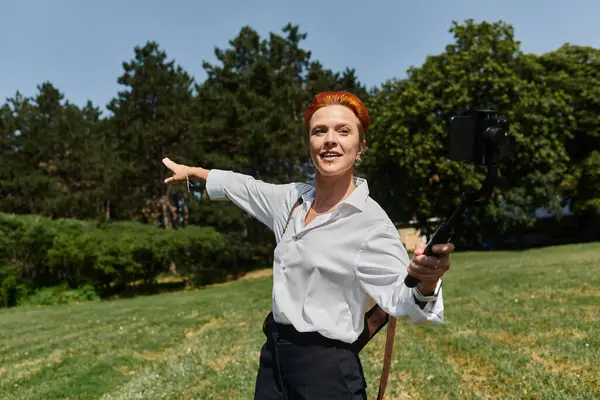 A woman with red hair smiles at the camera as she takes a selfie on a sunny campus. — Stock Photo