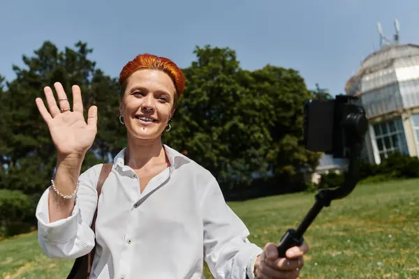 A woman with red hair smiles and waves at the camera. — Stock Photo