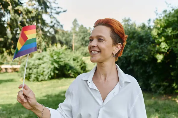 A teacher in a white shirt smiles as she holds a rainbow flag on a sunny campus. — Stock Photo