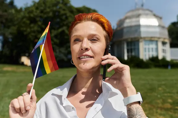 Red-haired teacher holds rainbow flag, talks on phone near college — Stock Photo