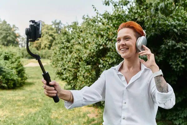 Une femme en chemise blanche sourit en enregistrant une vidéo avec un selfie stick à l'extérieur. — Photo de stock
