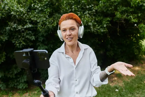 A woman in a white shirt records a video with a smartphone while wearing headphones. — Stock Photo