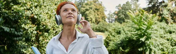 A woman wearing headphones walks through a leafy campus. — Stock Photo