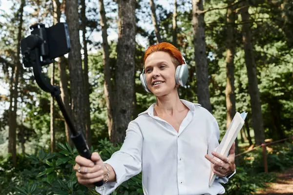 A teacher with red hair takes a selfie with a selfie stick while walking through a forest. — Stock Photo