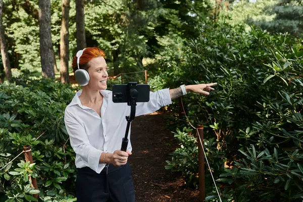 Young woman in white shirt and black pants chats on phone with a selfie stick on campus — Stock Photo