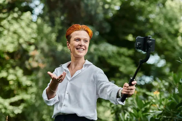 Un insegnante sorride mentre registra un video nella lussureggiante cornice verde di un campus. — Foto stock