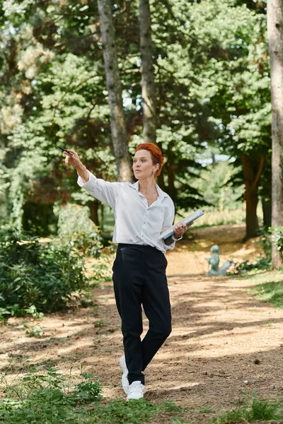 A woman in a white shirt and black pants points something out in a wooded area. — Stock Photo